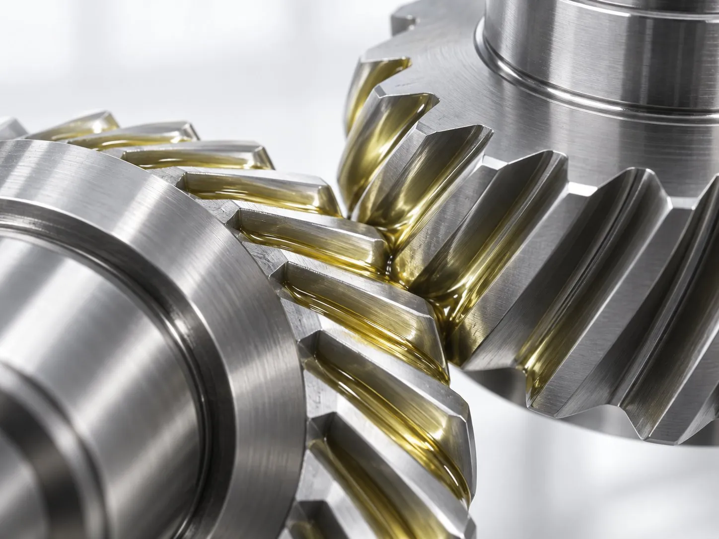 Two polished steel gears meshing, coated in a clear pale-yellow lubricant film